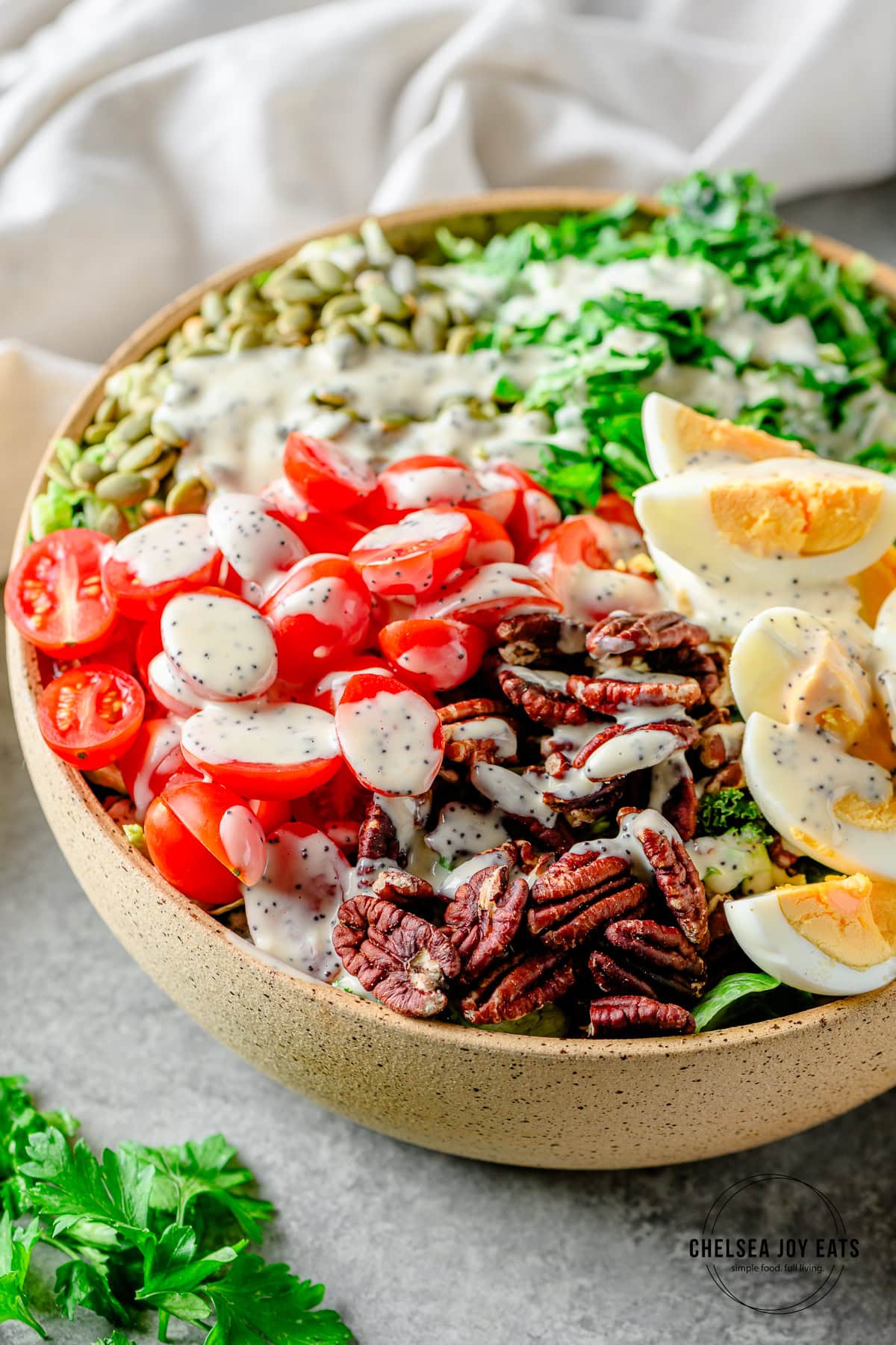 Tomatoes, pecans, and hard-boiled eggs on top of a chopped kale salad and drizzled in lemon tahini poppyseed dressing.