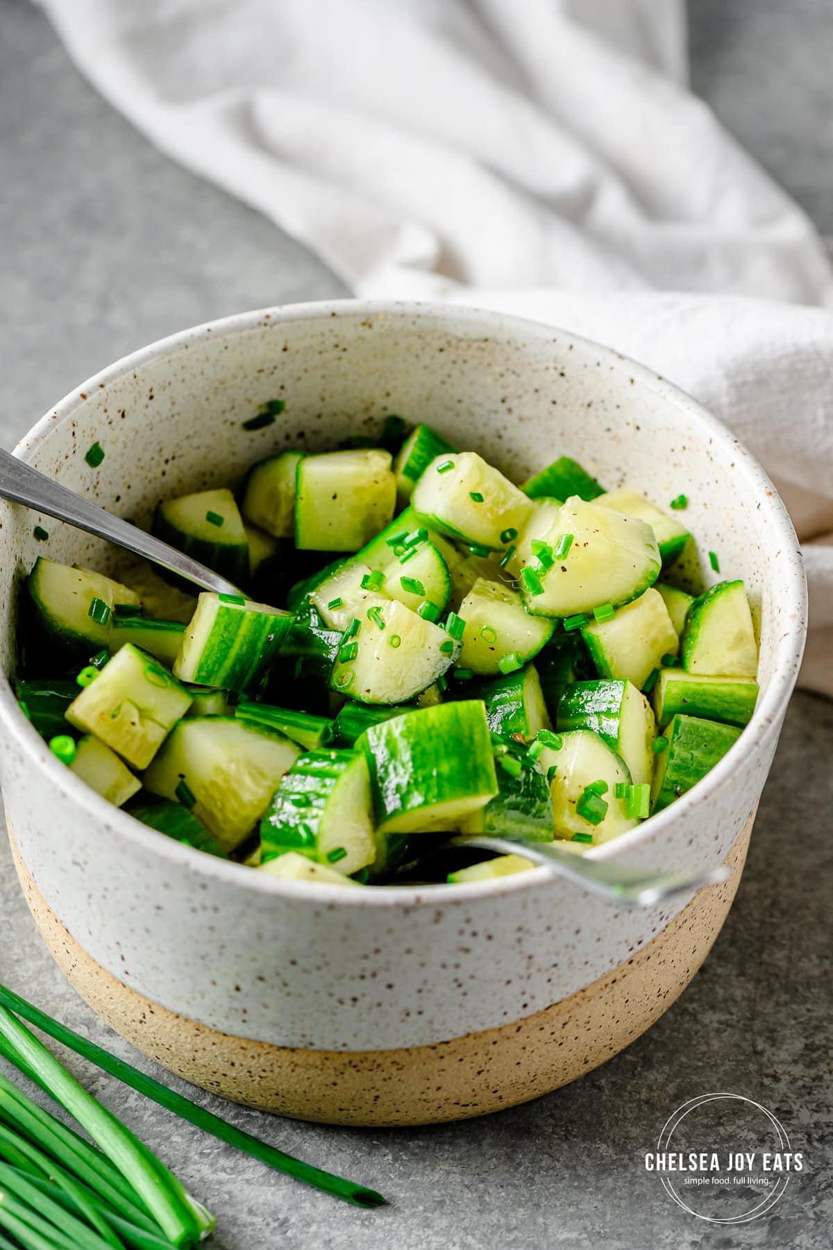 Cucumber salad tossed with vinaigrette and chives in a ceramic bowl with two forks.