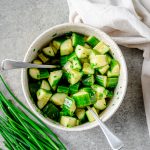 Chopped cucumber salad with chives in a pottery bowl with two forks.