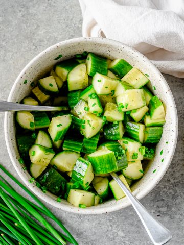 Chopped cucumber salad with chives in a pottery bowl with two forks.