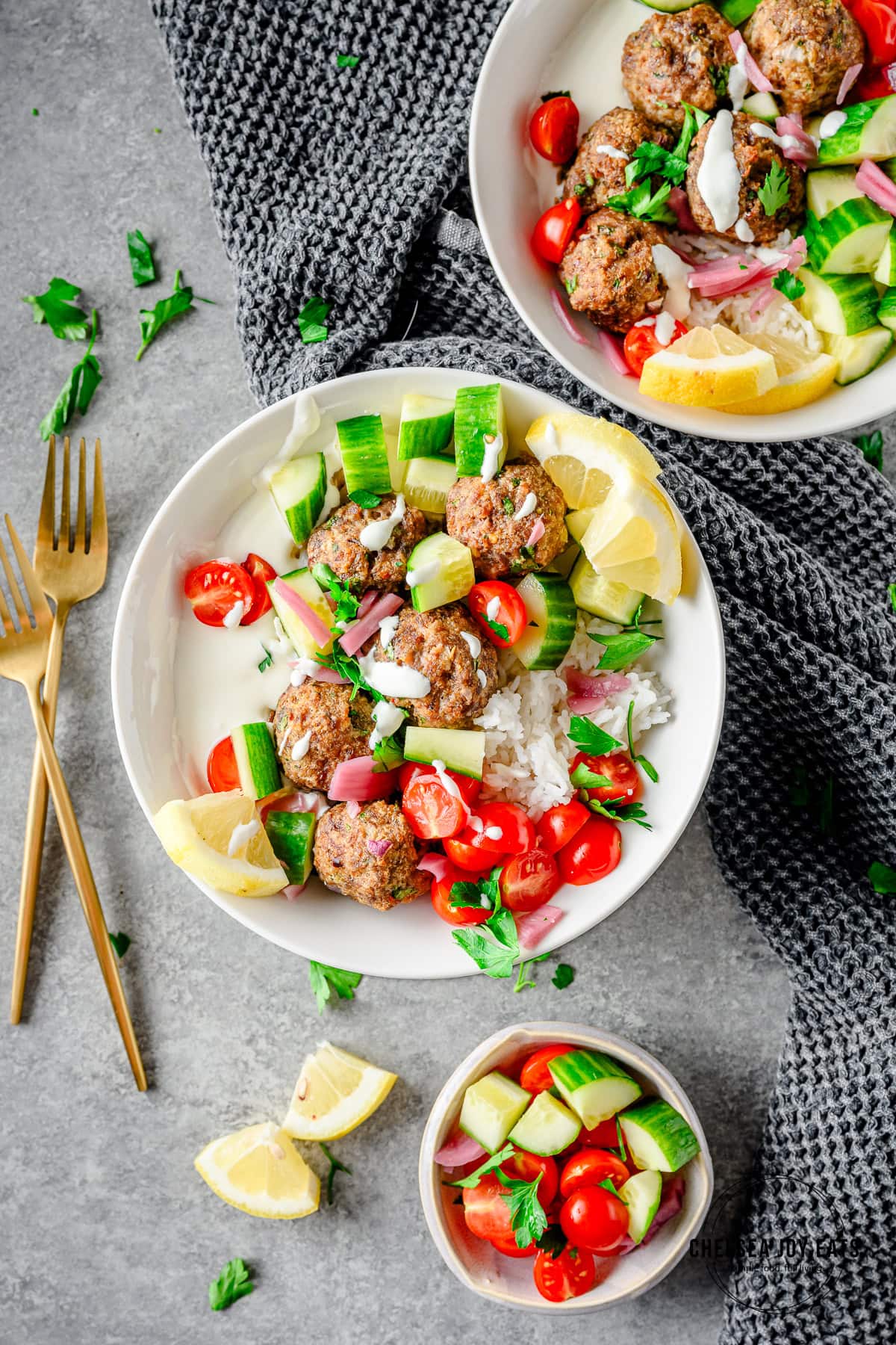 Bowl with rice, whipped feta, beef and lamb meatballs, and tomatoes and cucumber with additional bowls and forks besides.