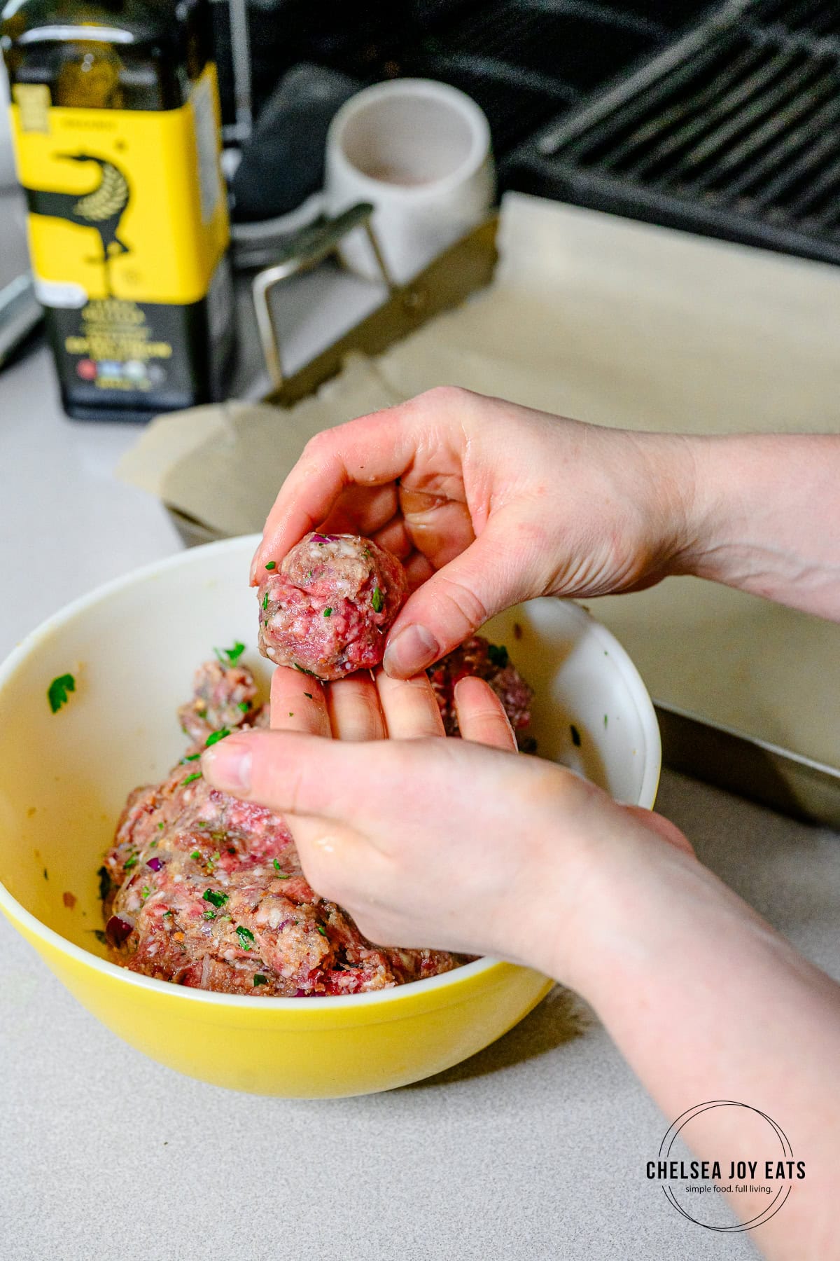 A person forming meatballs from a mixing bowl of meat mixture with their hands.