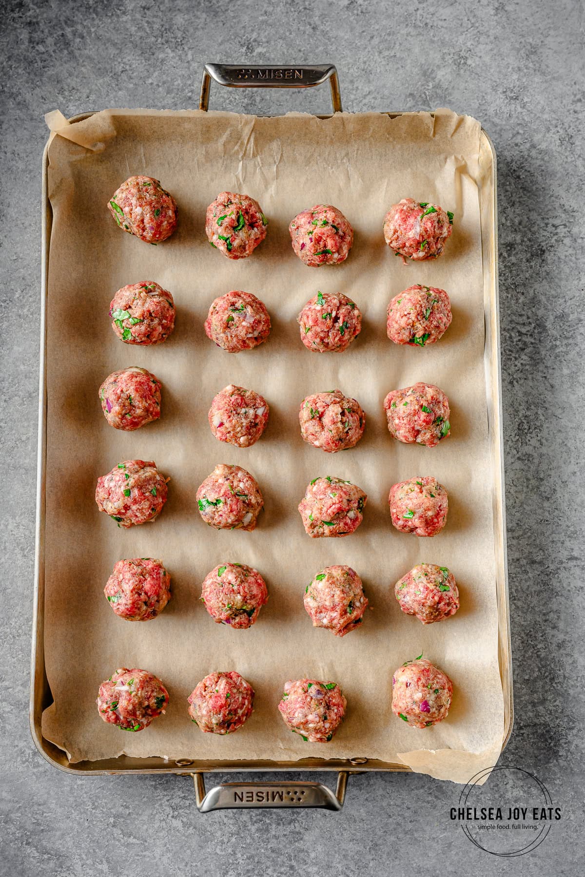 Uncooked lamb and beef meatballs lined up on a baking sheet lined with parchment paper.