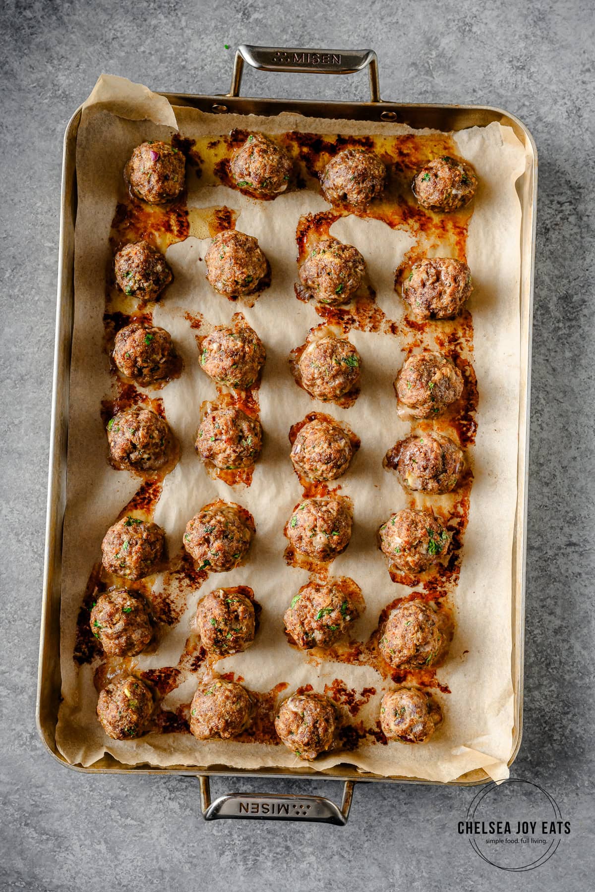 Cooked beef and lamb meatballs on a parchment paper-lined baking sheet.