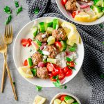 Bowl with rice, whipped feta, beef and lamb meatballs, and tomatoes and cucumber with additional bowls and forks besides.