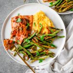 Plate with ginger miso salmon, polenta, and roasted green beans with a fork taking a bite out of the salmon.