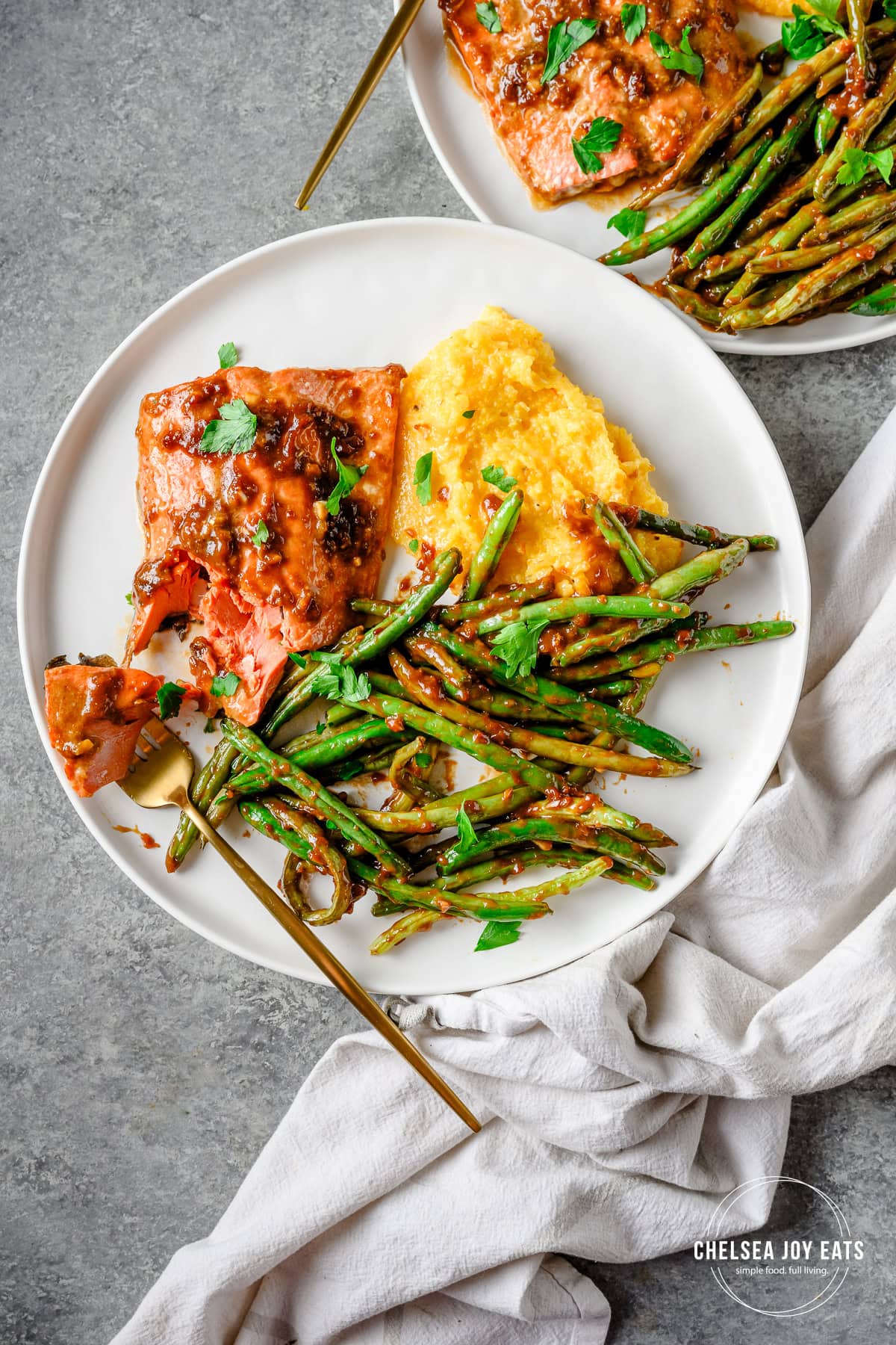 Plater with ginger miso salmon, polenta, and roasted green beans with a fork taking a bite out of the salmon.