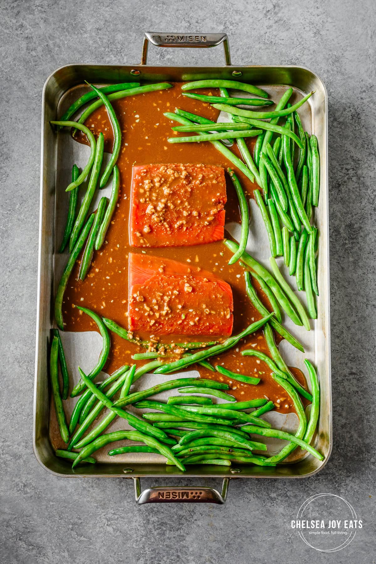 Green beans and salmon on a sheet pan with gingo miso sauce poured overtop.
