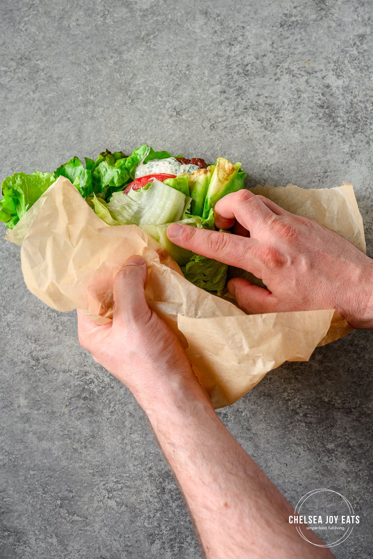 Person using parchment paper to help guide lettuce wrapping for a bunless burger with toppings.