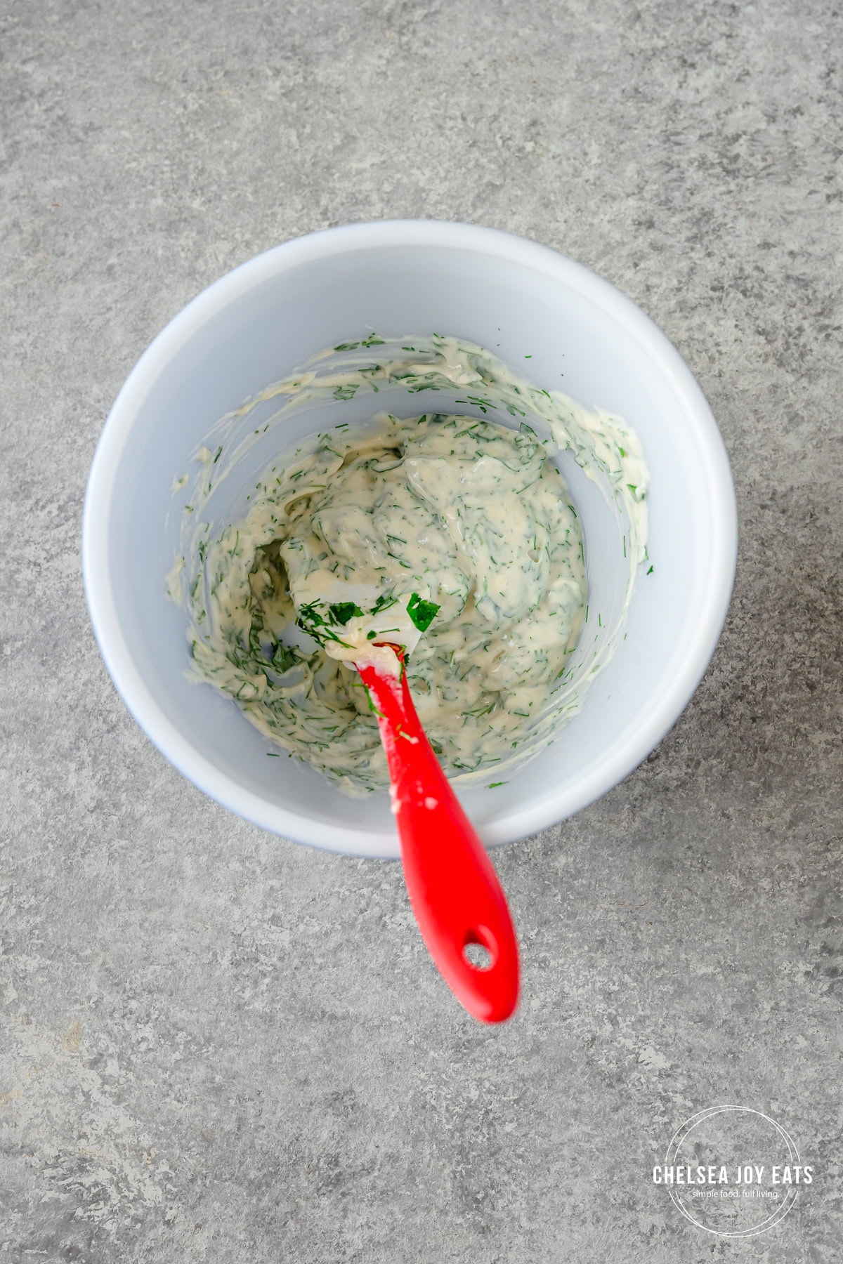 Cilantro dill mayonaisse in a small cermic dish with a small spatula stirring.