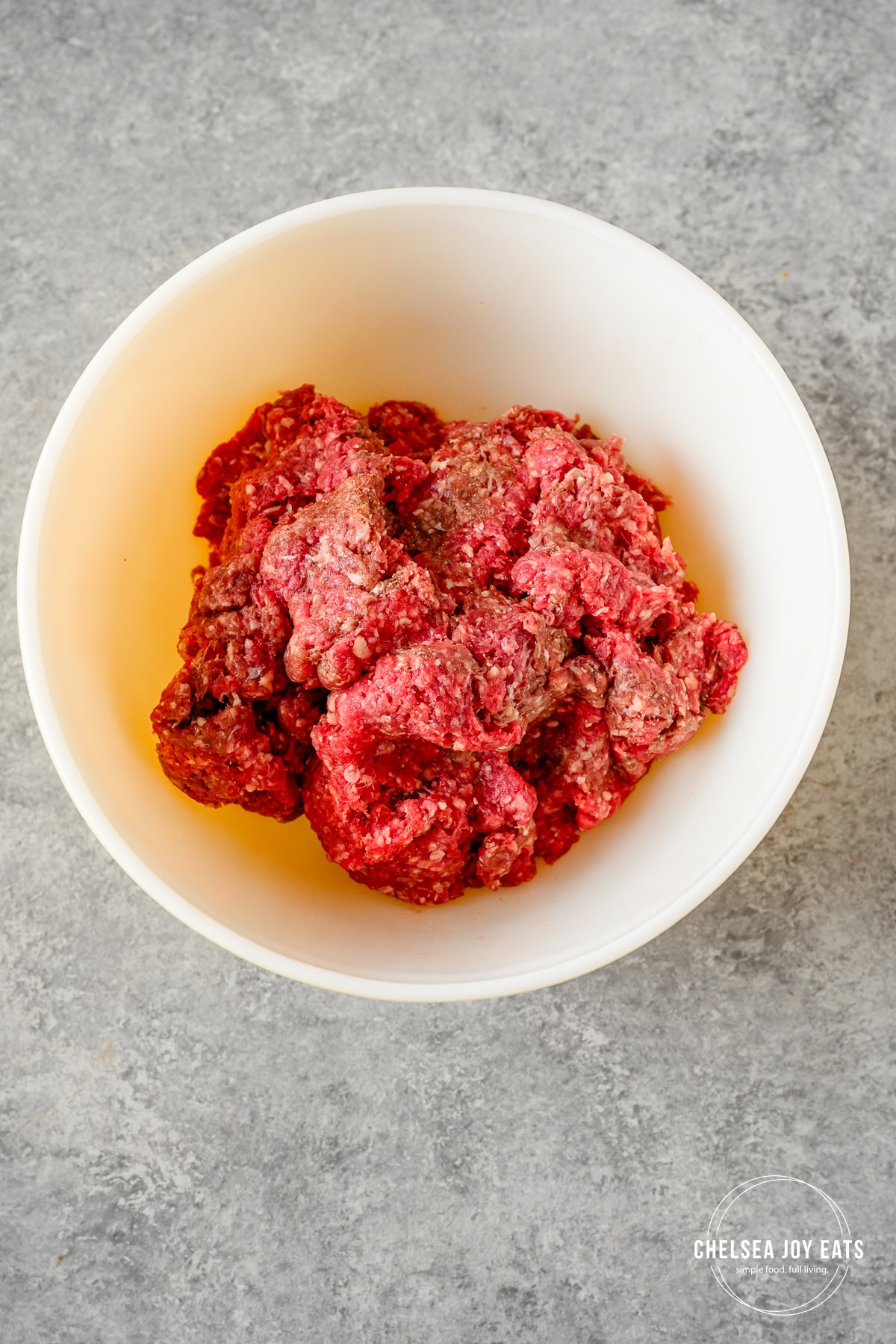 Ground beef mixed with salt and pepper in a large ceramic bowl.
