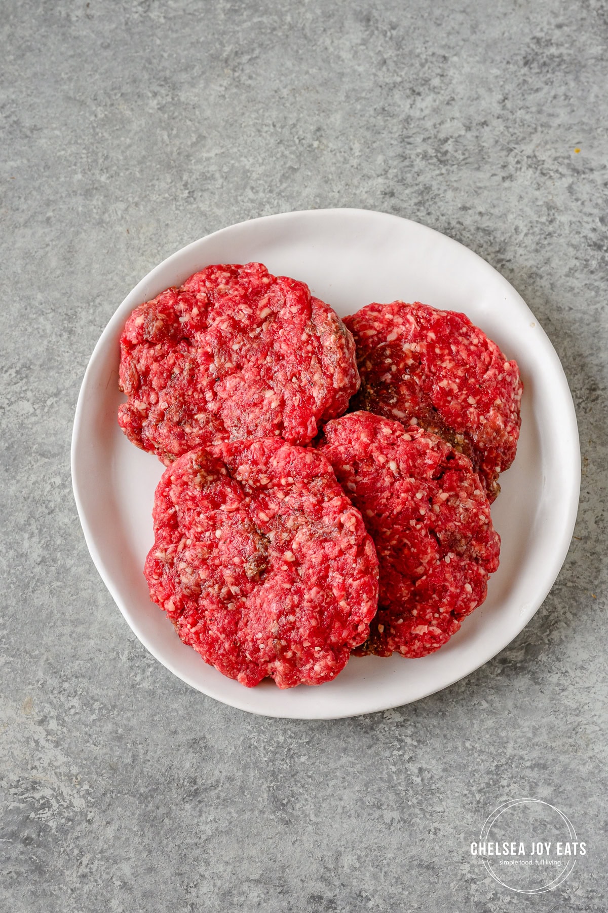 Raw hand-formed burger patties on a white plate.