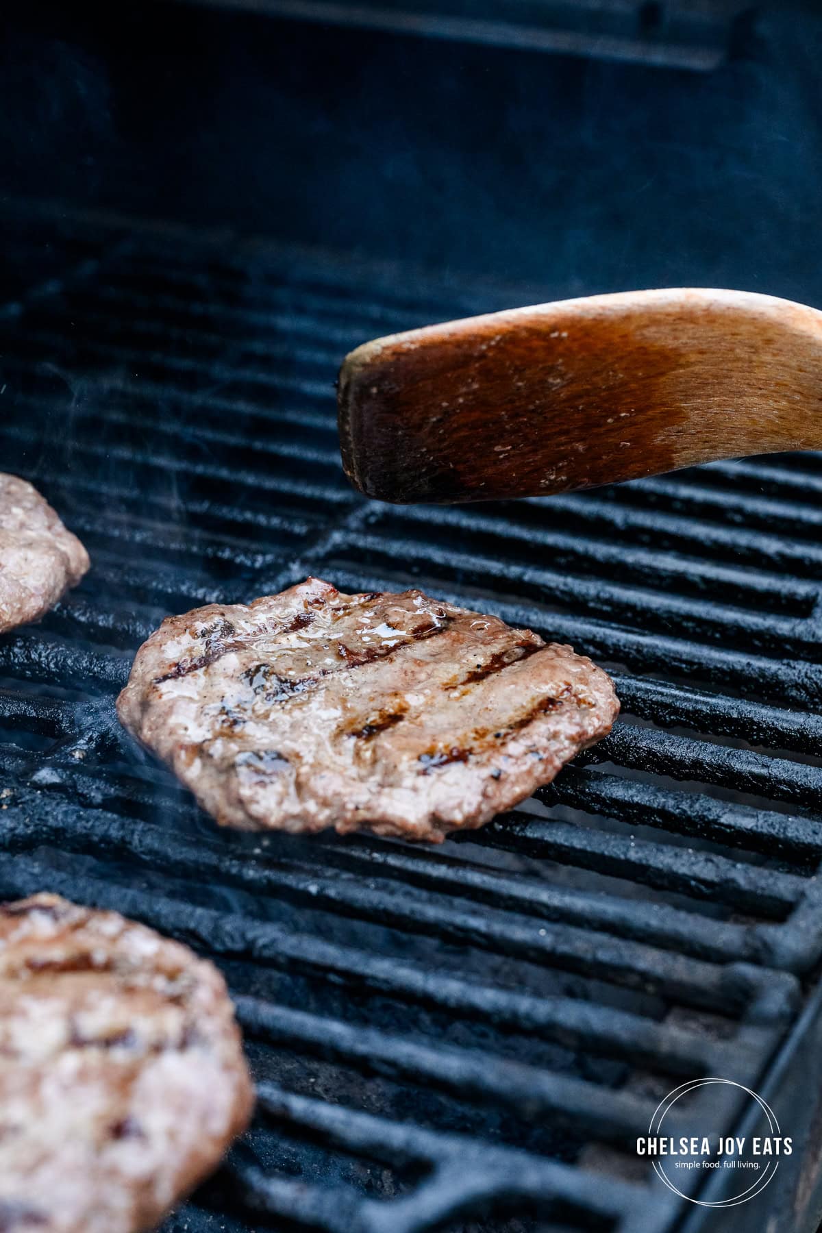 Burger patties being flipped on a grill with a wooden spatula.