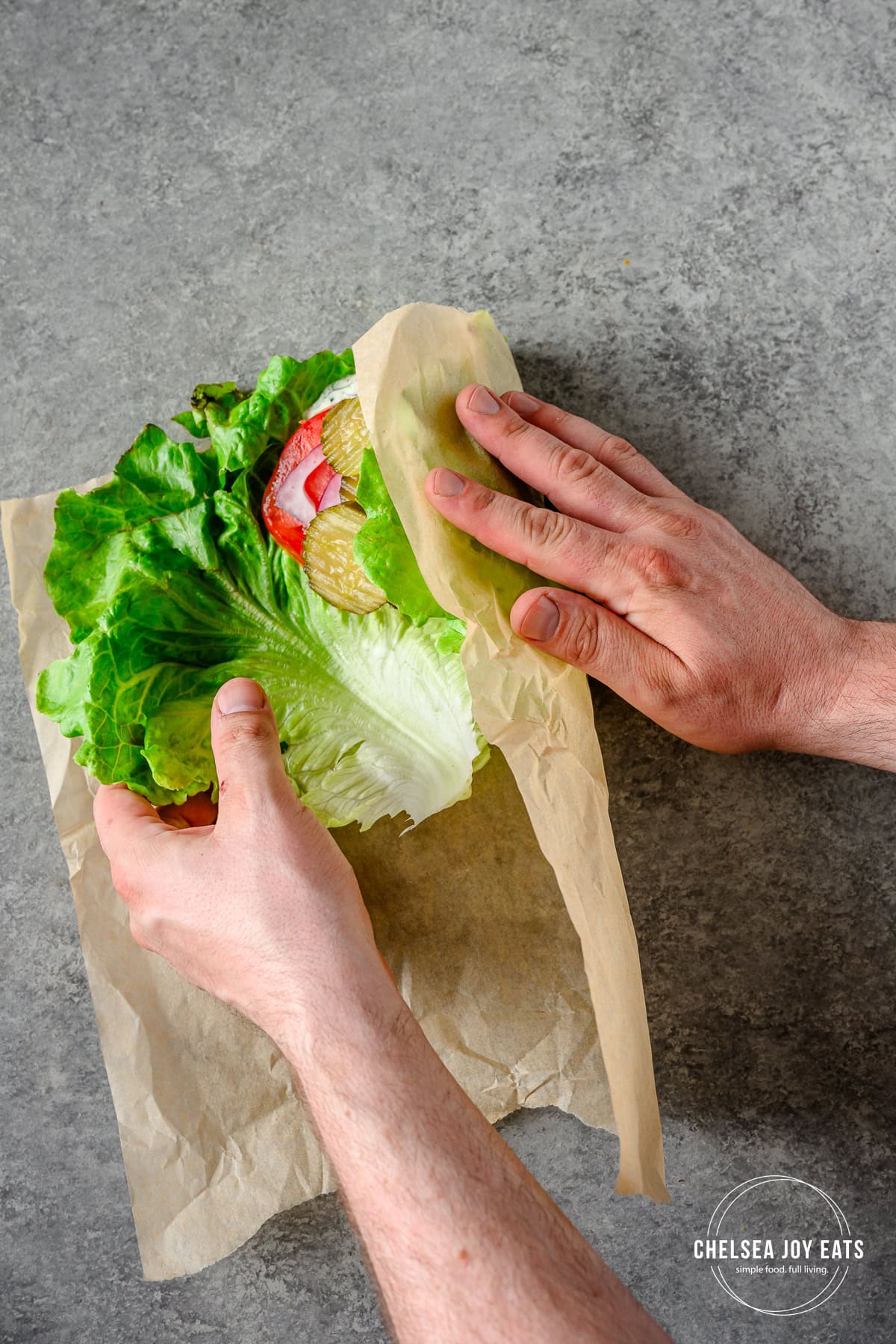 Person using parchment paper to fold lettuce over a bunless burger.
