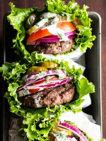 Lettuce-wrapped bunless burgers stacked in a loaf pan against a dark background.