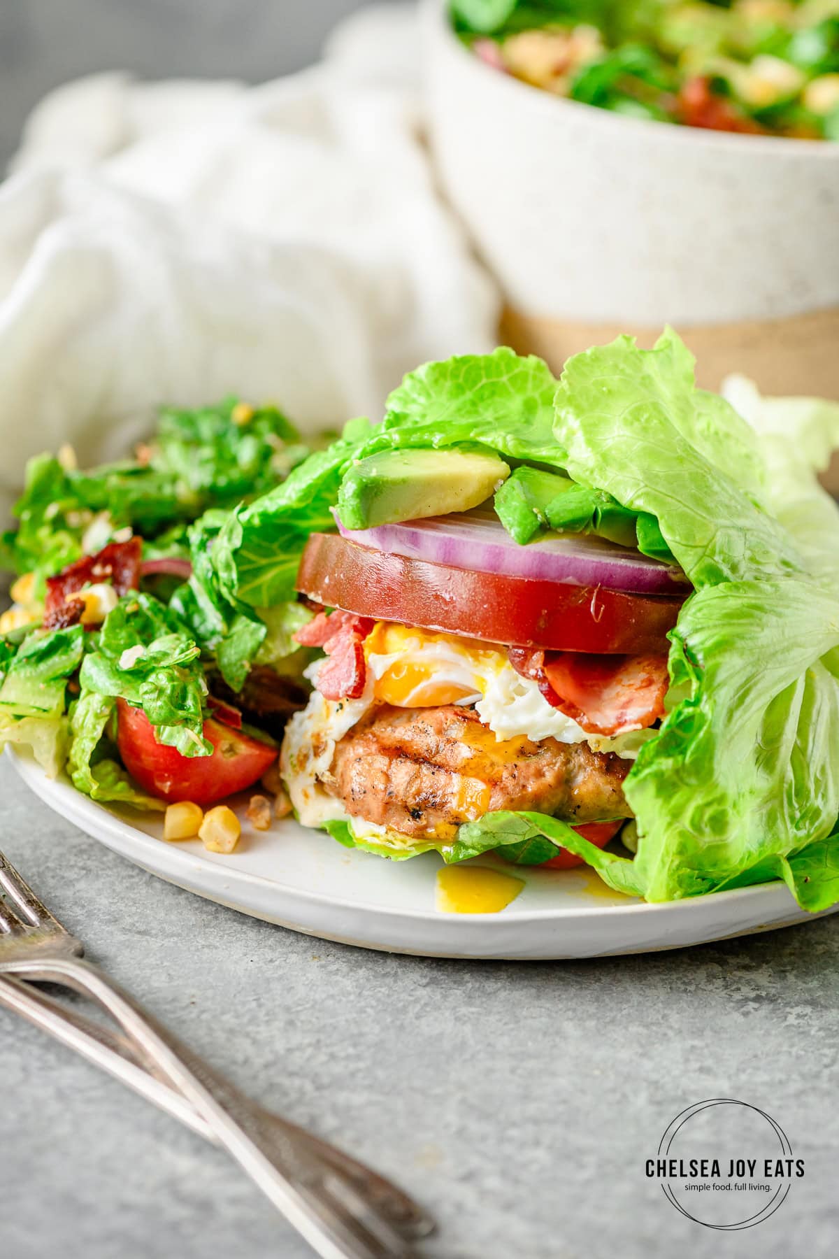 Lettuce-wrapped gluten free chicken Cobb burger served on a plate with a salad.