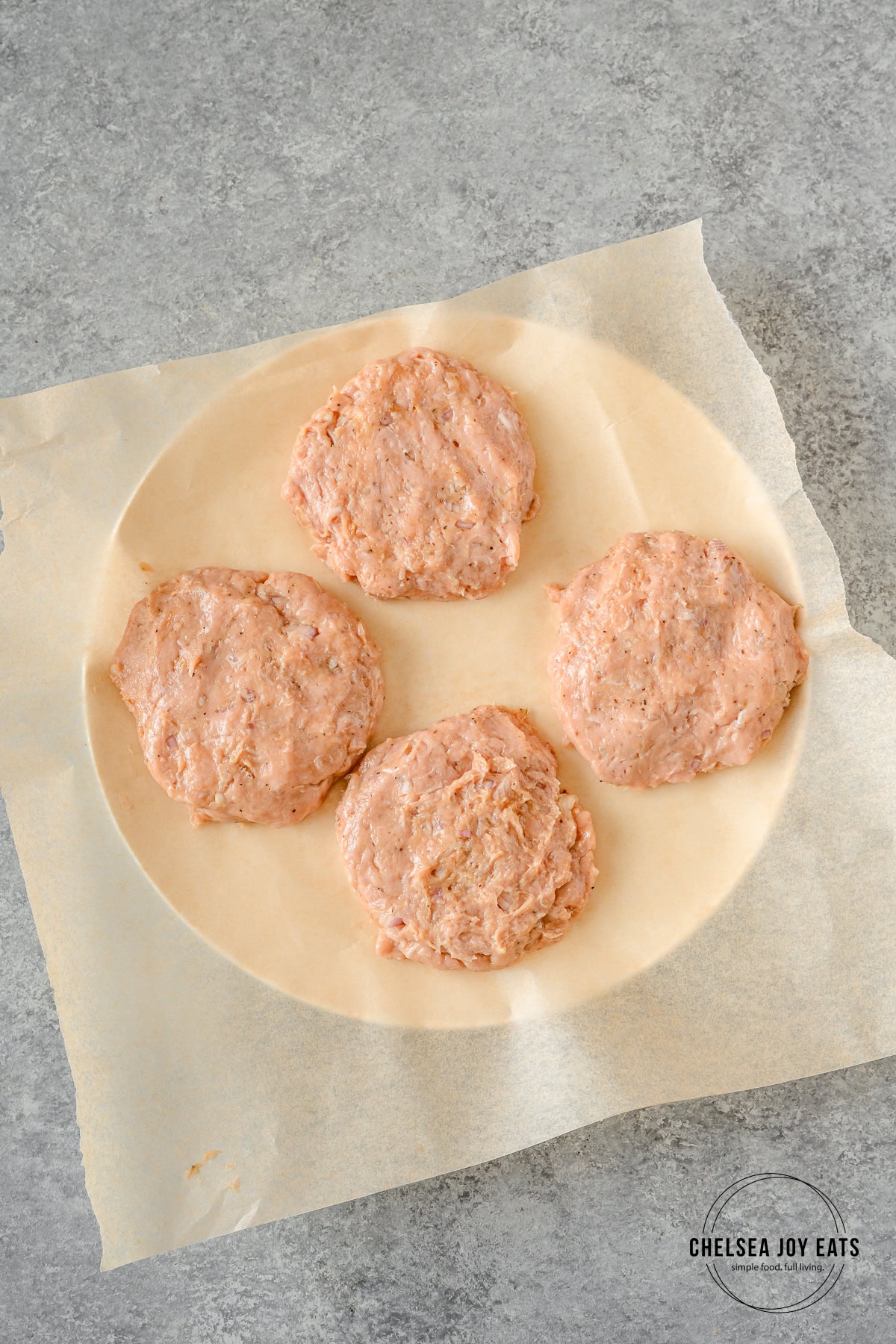 Raw chicken patties on a piece of parchment paper.