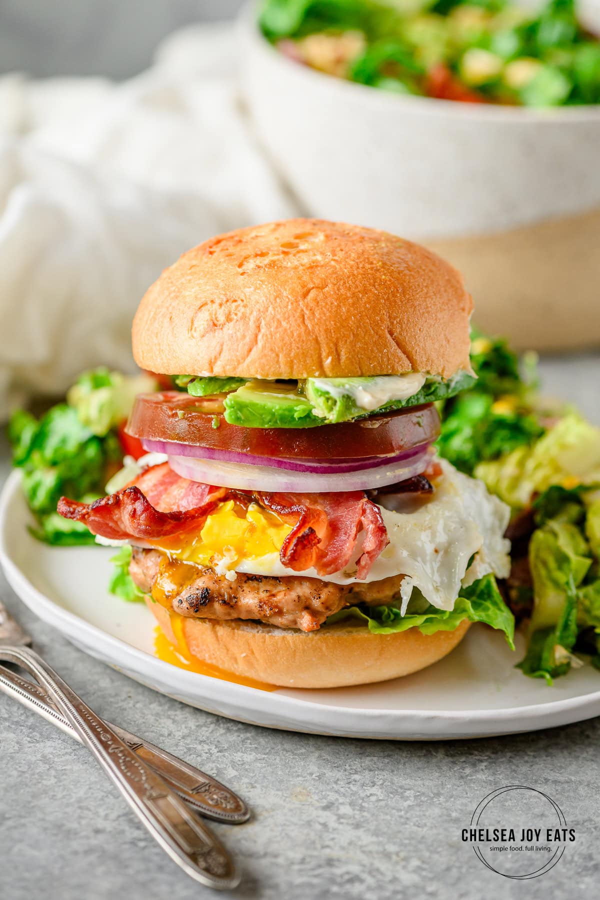 Assembled gluten free chicken cobb burger served on a gluten free bun on a white plate.