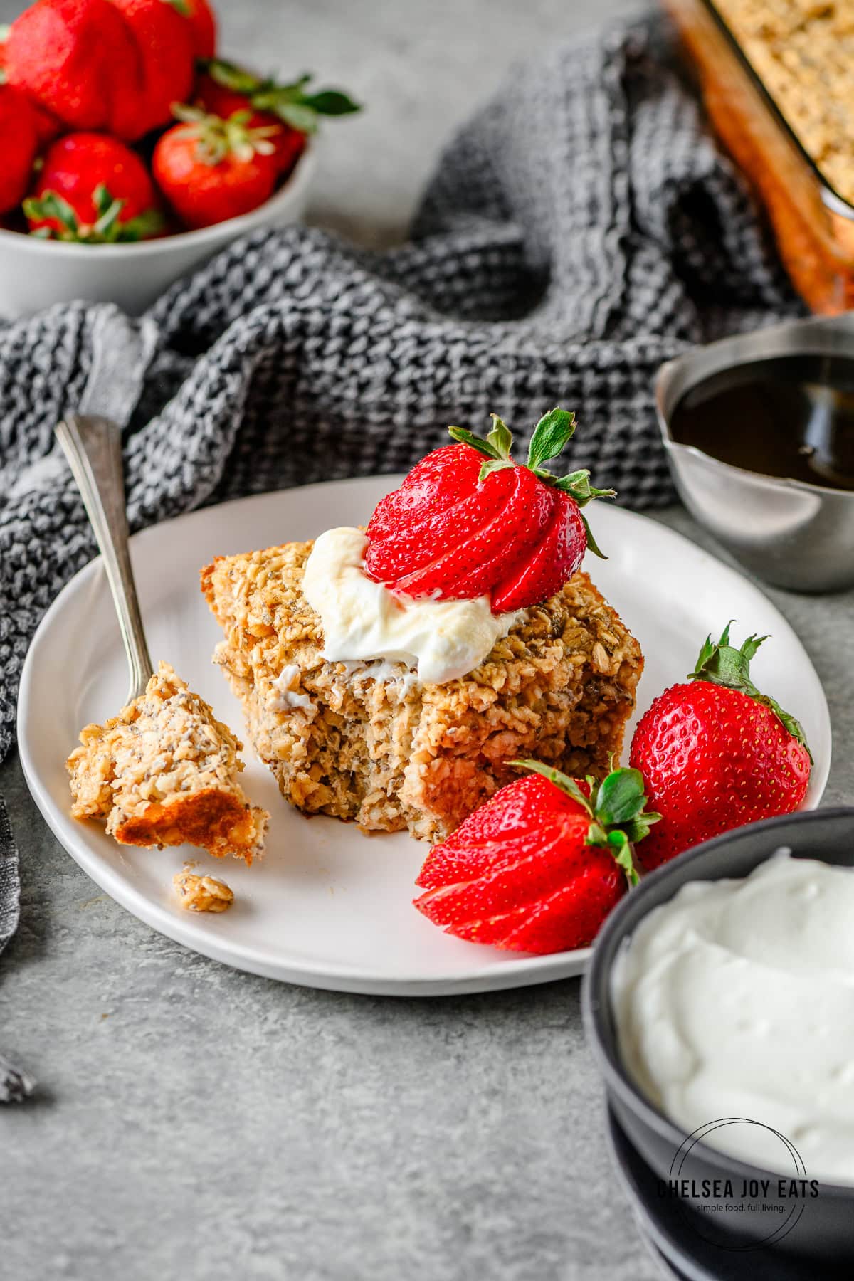 Serving of cottage cheese baked oats on a white plate garnished with Greek yogurt and fresh strawberries, with a fork taking a bite out.