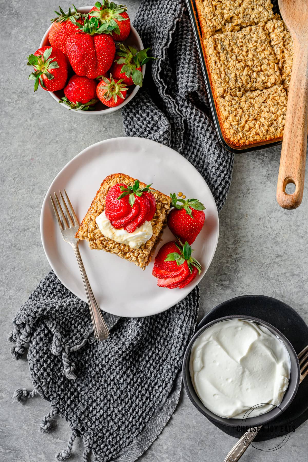 Serving of gluten free baked oatmeal topped with Greek yogurt and fresh strawberries, with a full dish of baked oats and dished with yogurt and strawberries besides.