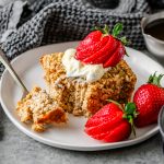 Serving of cottage cheese baked oats on a white plate garnished with Greek yogurt and fresh strawberries, with a fork taking a bite out.