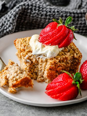 Serving of cottage cheese baked oats on a white plate garnished with Greek yogurt and fresh strawberries, with a fork taking a bite out.