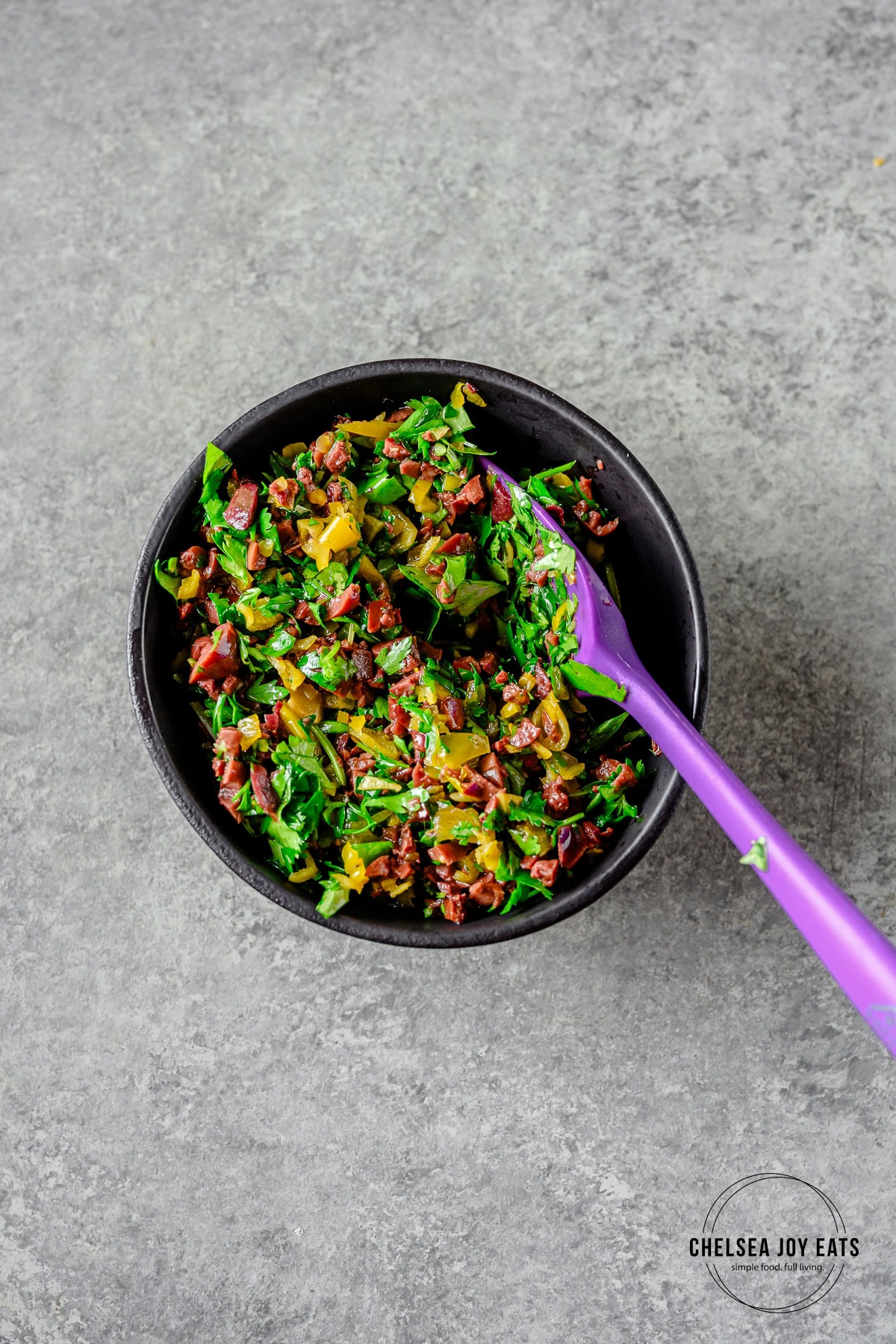Kalamata olive herb relish in a small bowl stirred with a spatula.