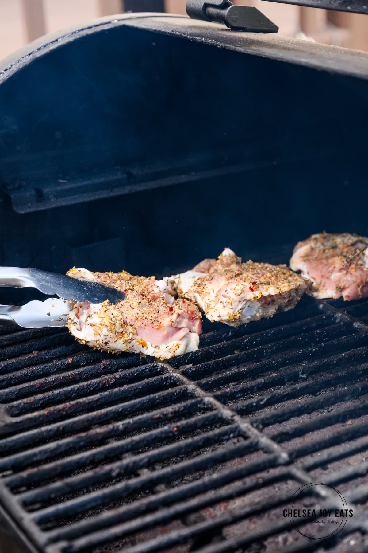 Chicken thighs being added skin side down onto a grill for cooking.