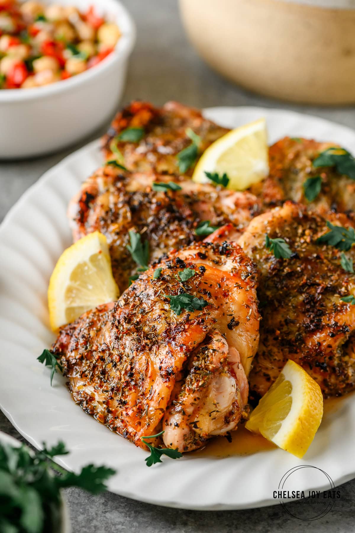 Serving platter with Greek Grilled Chicken Thighs garnished with parsley and lemon wedges.