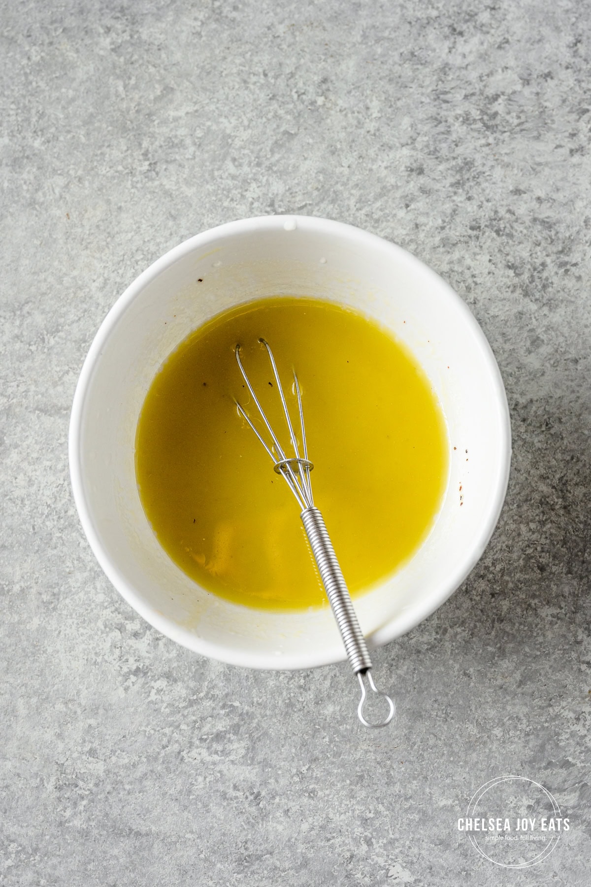 Lime vinaigrette whisked in a small white bowl on a light countertop.