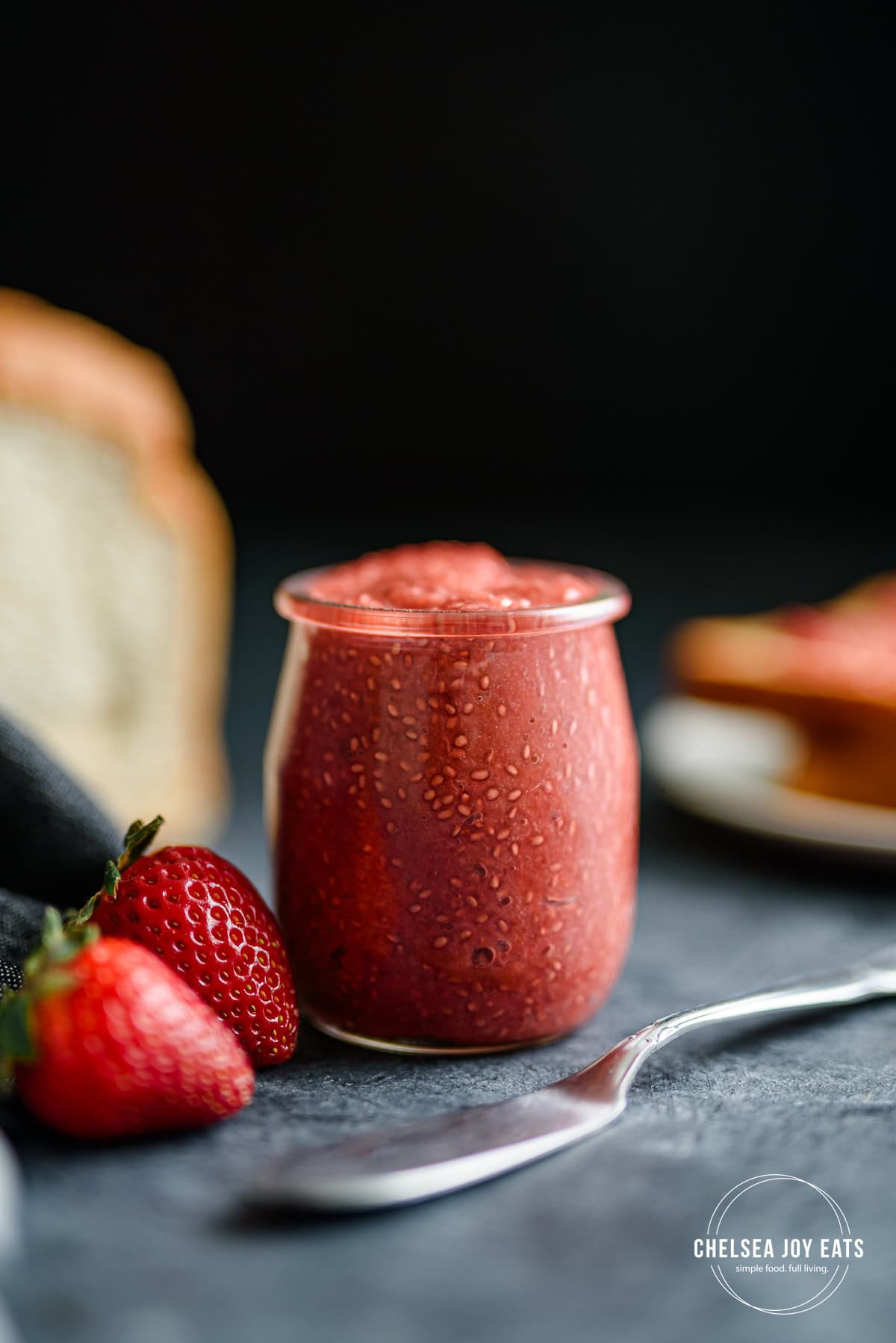 Jar of strawberry rhubarb chia seed jam with spoon and strawberries.