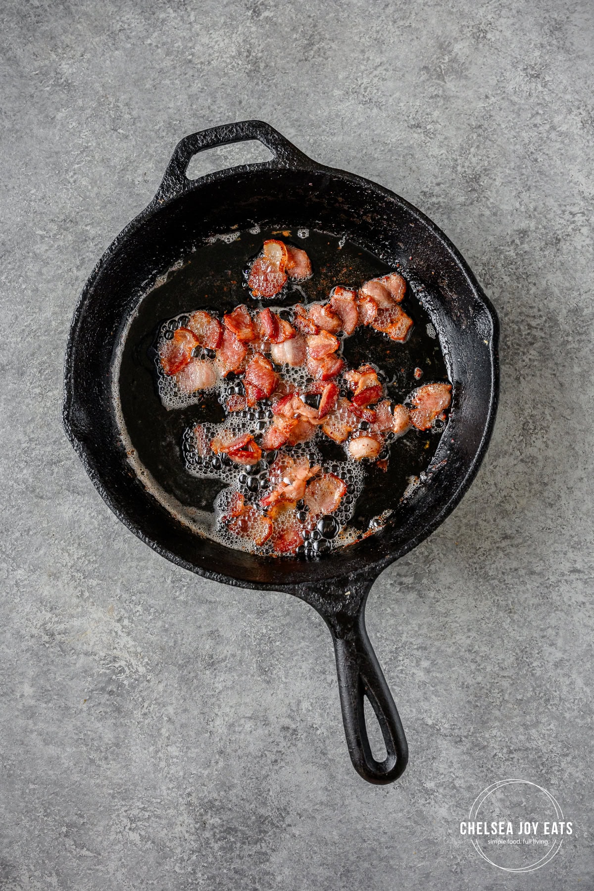 Bacon pieces cooking in a cast iron skillet.