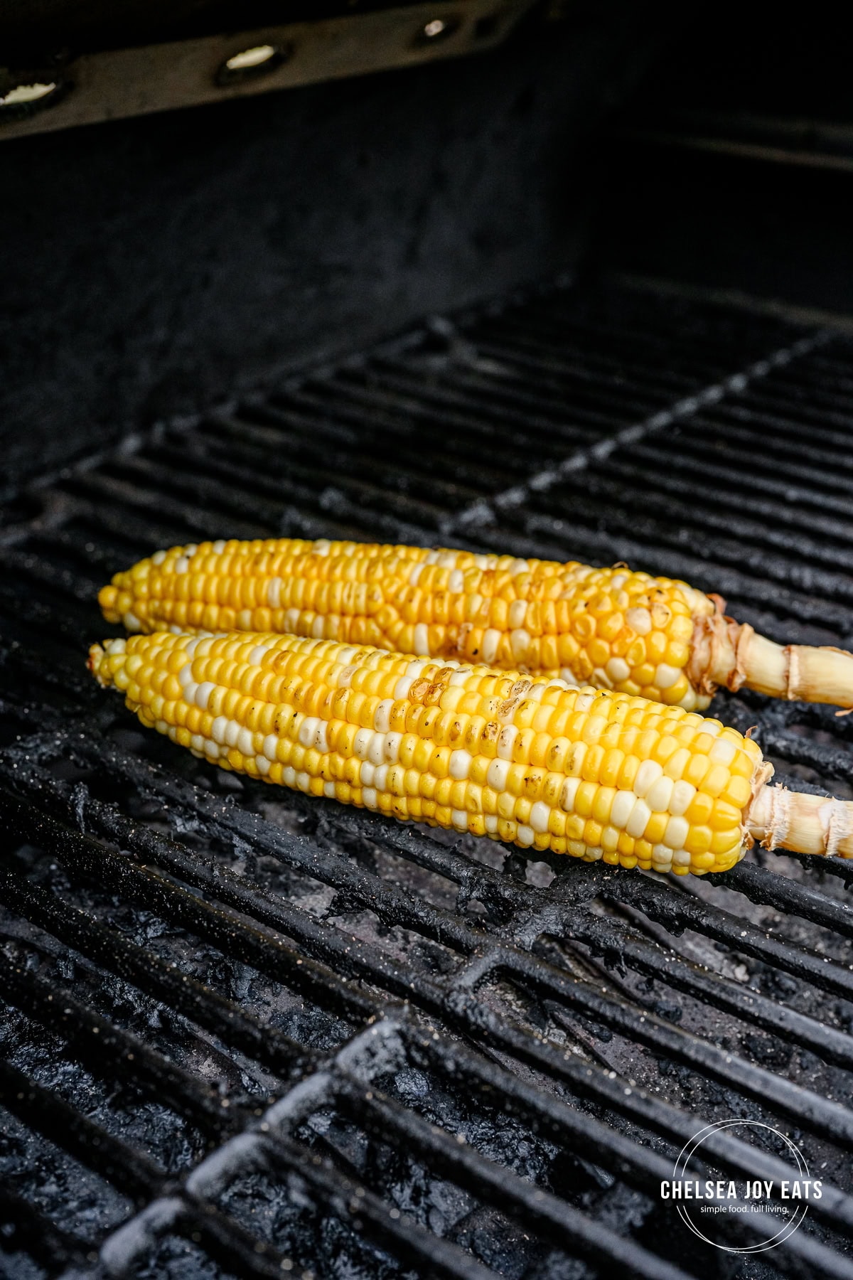 Two ears of fresh corn cooking on a pellet grill.