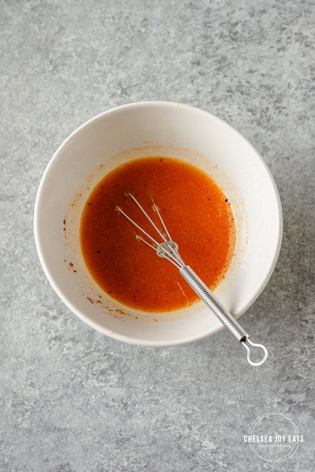 Smokey bacon vinaigrette in a small ceramic bowl with a small whisk on a grey countertop.