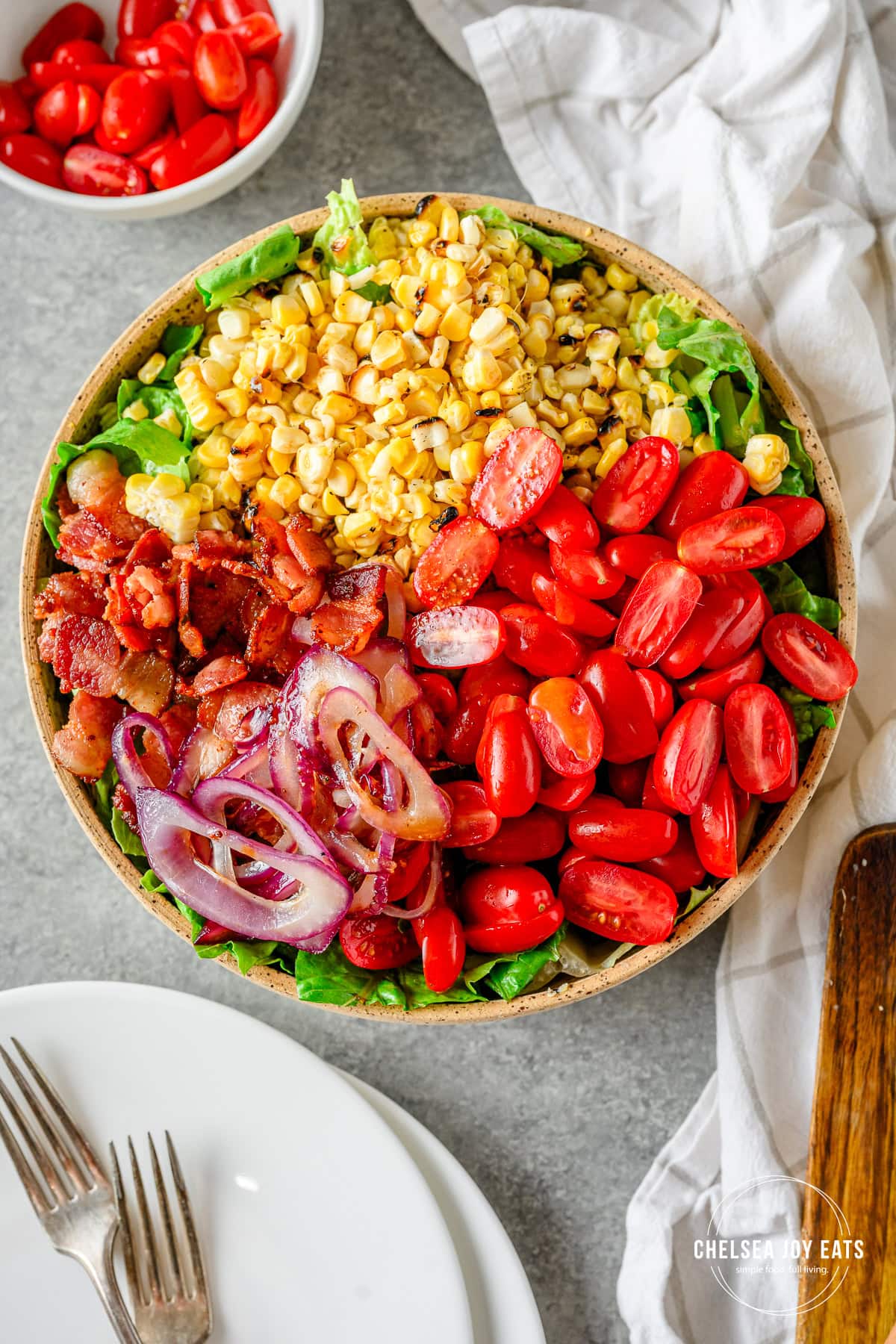 BLT-inspired corn & tomato salad with corn, tomatoes, red onion, and bacon on a bed of romaine lettuce in a large bowl.