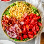 BLT-inspired corn & tomato salad with corn, tomatoes, red onion, and bacon on a bed of romaine lettuce in a large bowl.