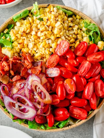BLT-inspired corn & tomato salad with corn, tomatoes, red onion, and bacon on a bed of romaine lettuce in a large bowl.