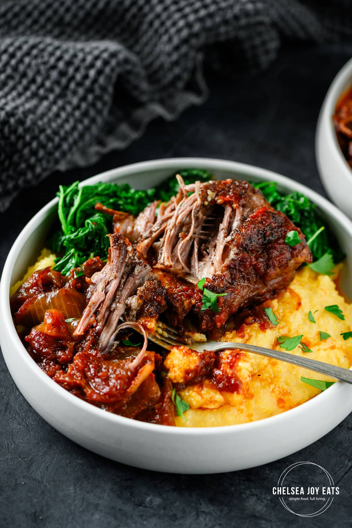 Braised tomato balsamic short rib portion served in a low bowl over polenta with kale on the side.