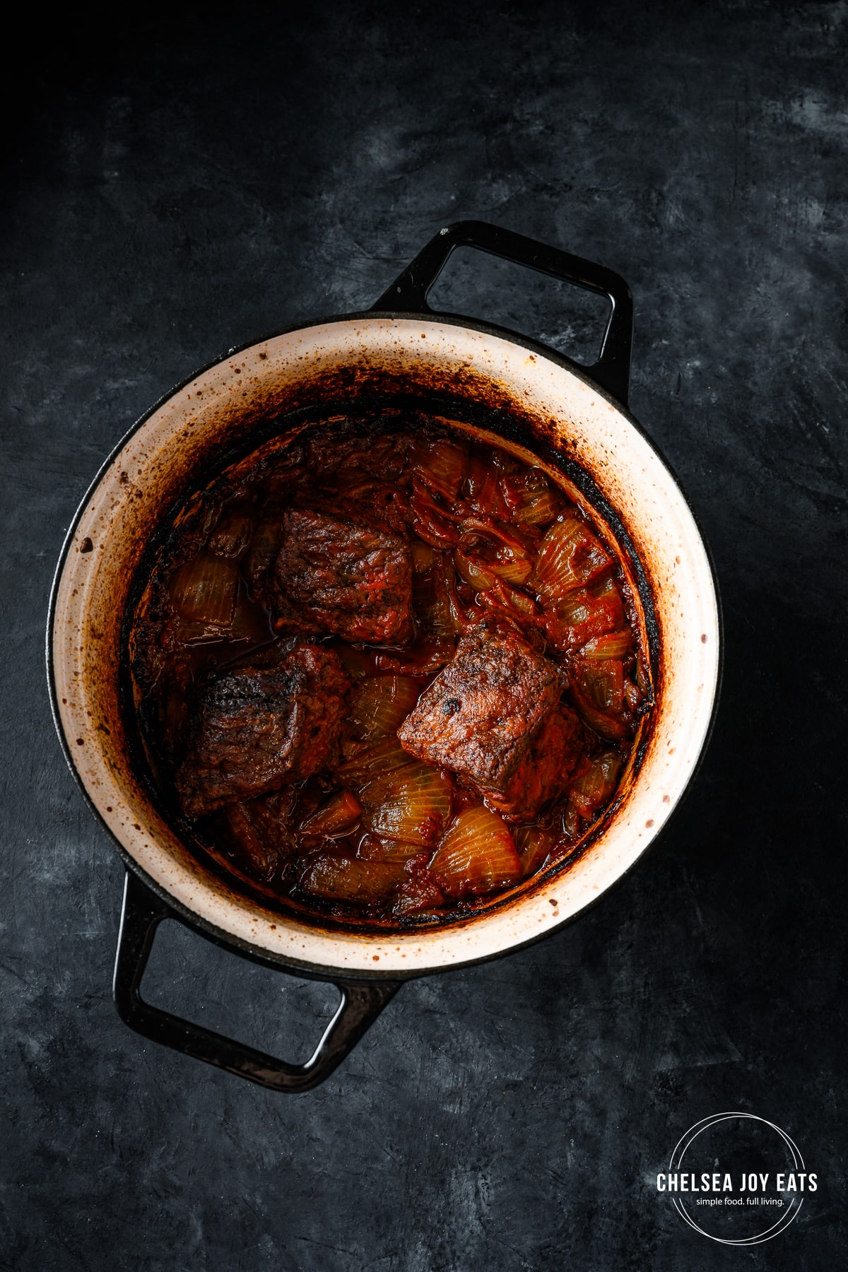 Seared beef short ribs added back to a Dutch oven with sautéed garlic, onions, balsamic vinegar, and crushed tomatoes.