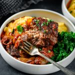 Braised tomato balsamic short rib portion served in a low bowl over polenta with kale on the side.