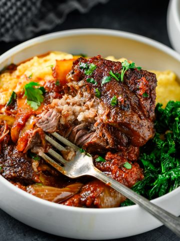 Braised tomato balsamic short rib portion served in a low bowl over polenta with kale on the side.