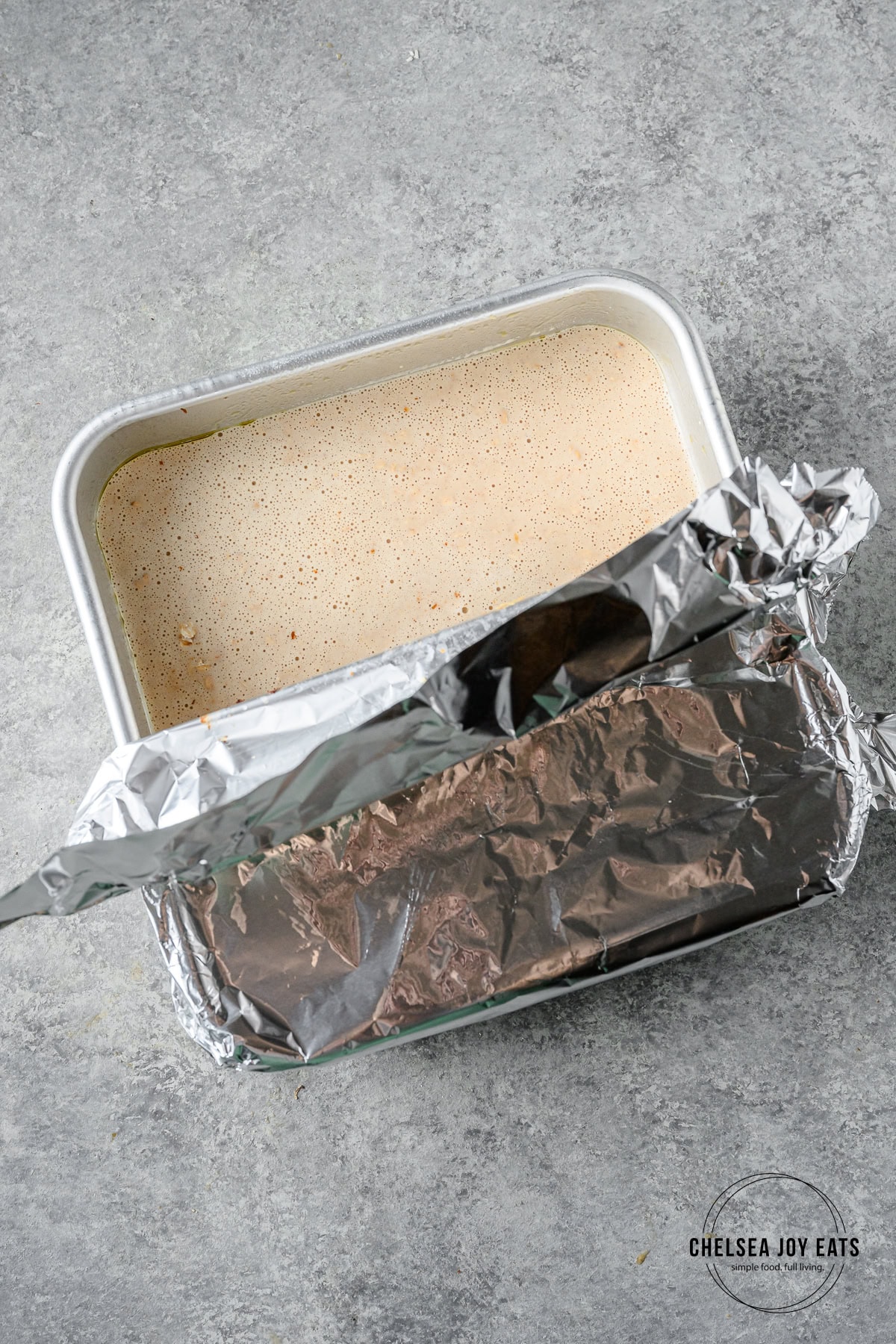 Unbaked banana bread oats in an 8x8 baking dish partially covered with tinfoil.