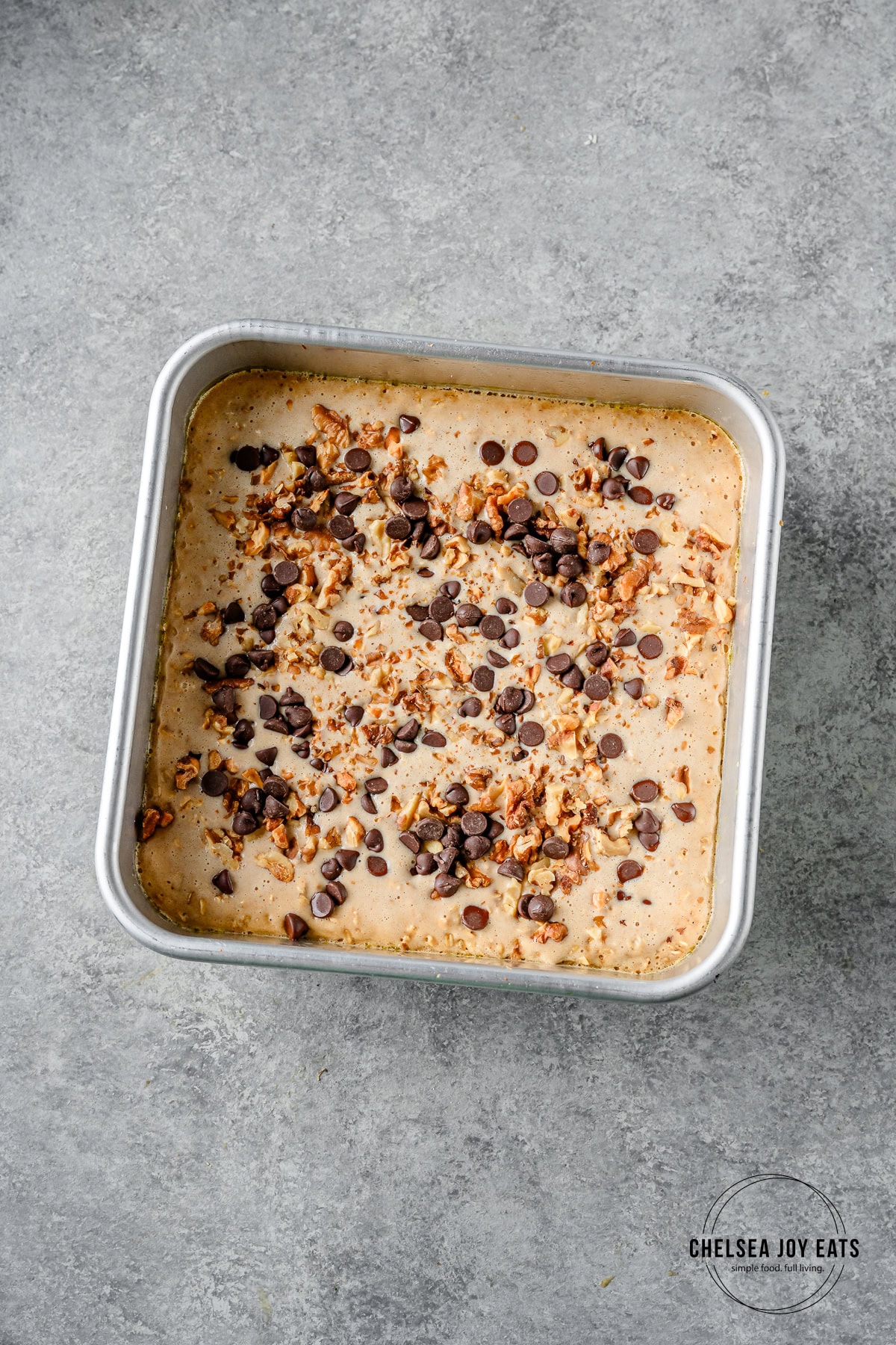 Partially baked banana bread oatmeal in an 8x8 baking dish with walnuts and chocolate chips sprinkled overtop.