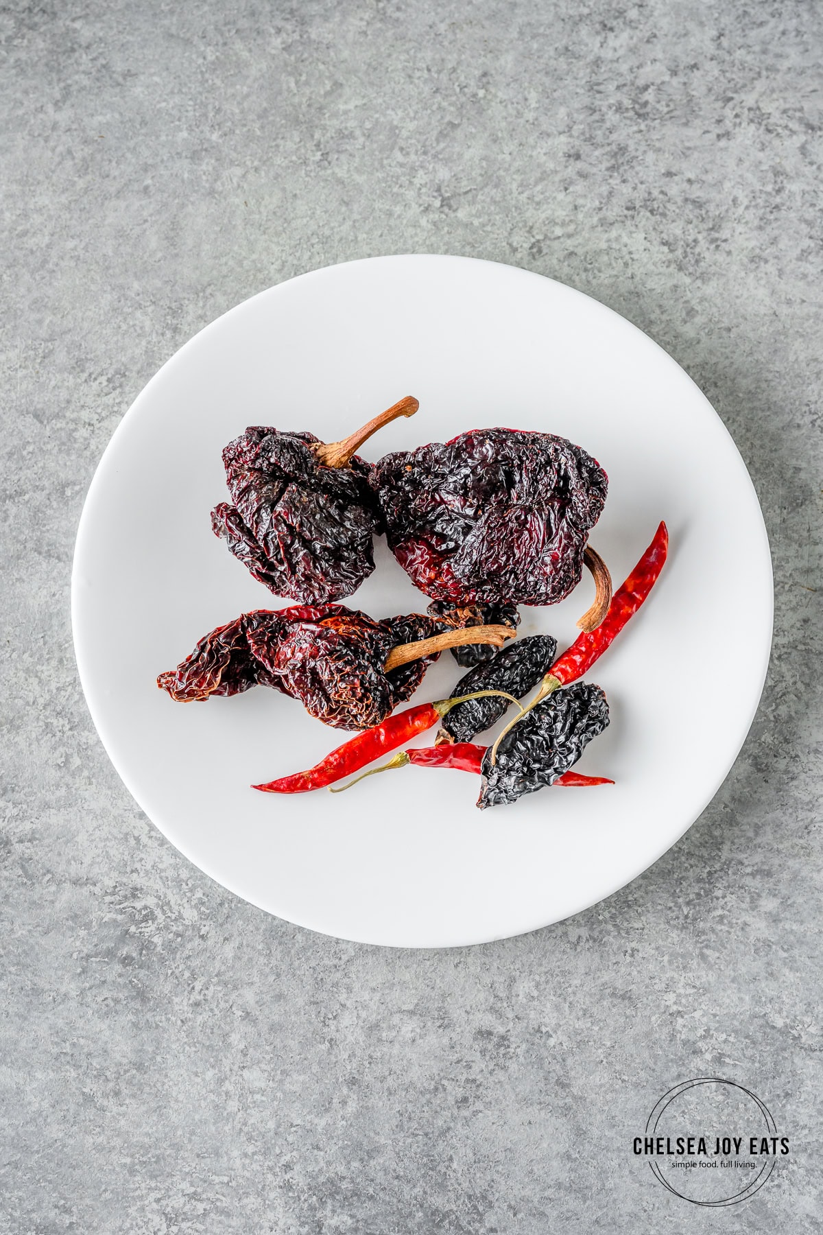 Dried chiles on a white plate against a grey countertop.