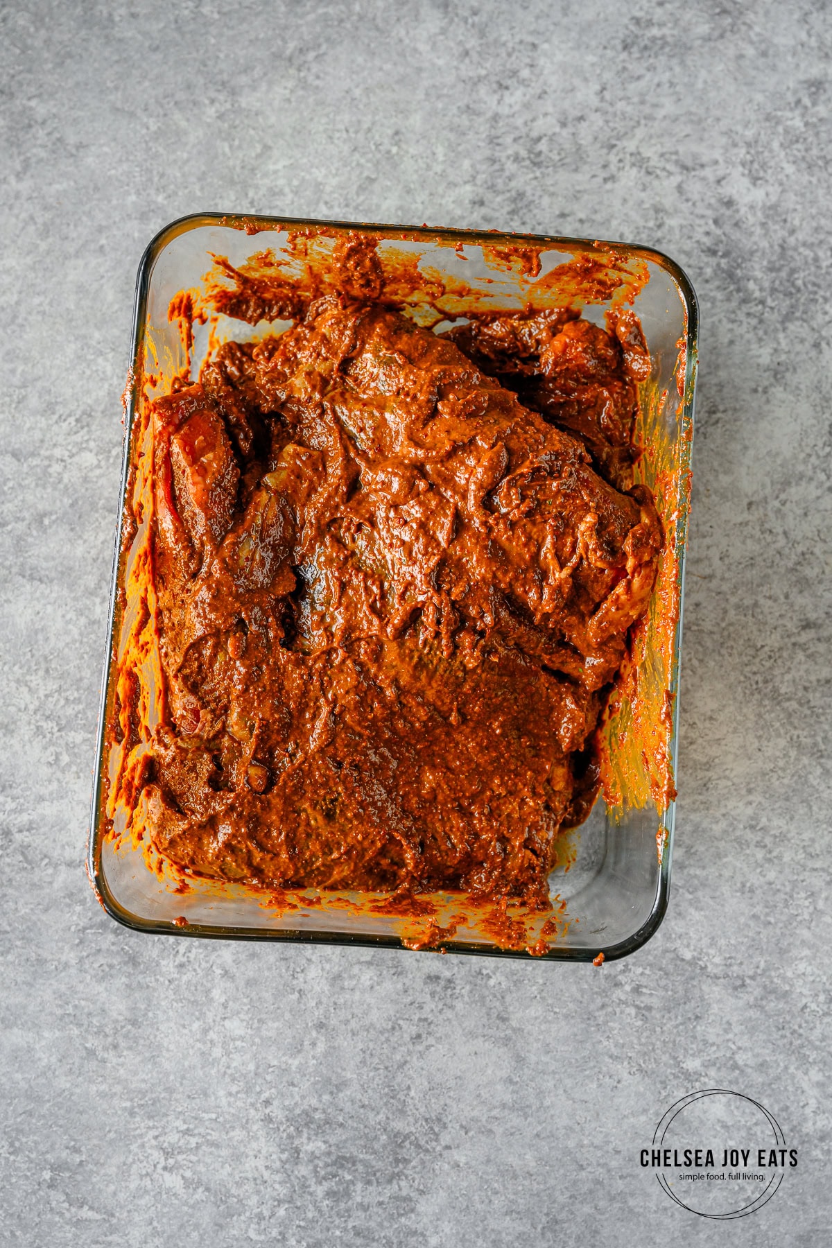Skirt steak slathered in carne asada marinade in a glass container.