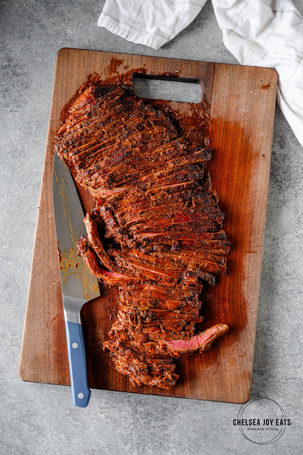 Cooked carne asada sliced thinly against the grain on a wooden cutting board with a chef's knife.