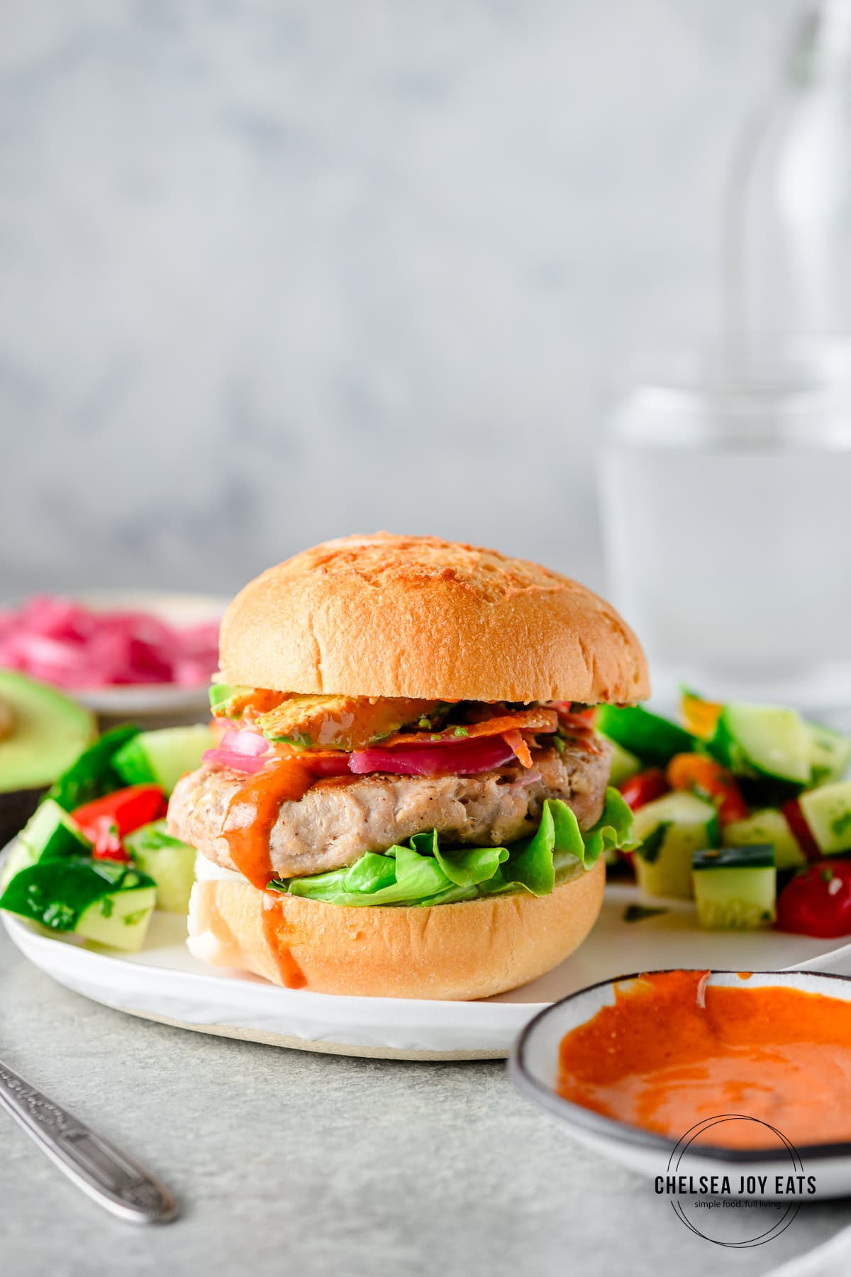 Homemade tuna burgers with pickles onions and sriracha mayo on a gluten free bun served on a plate with a salad.