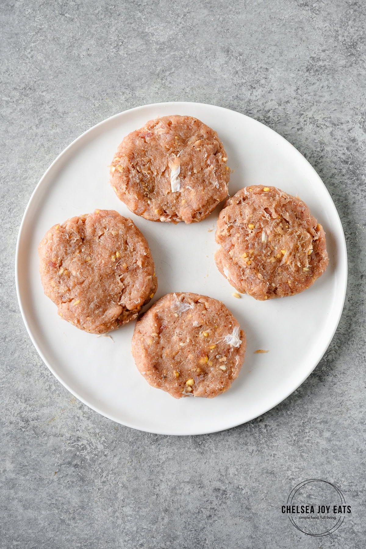 Patties formed from blended tuna on a white plate against a grey countertop.