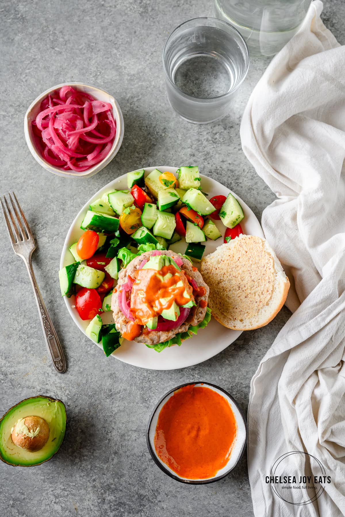 Assembled gluten free tuna burger on a gluten free bun with avocado, pickled onions, and sriracha mayo on a plate with a salad.