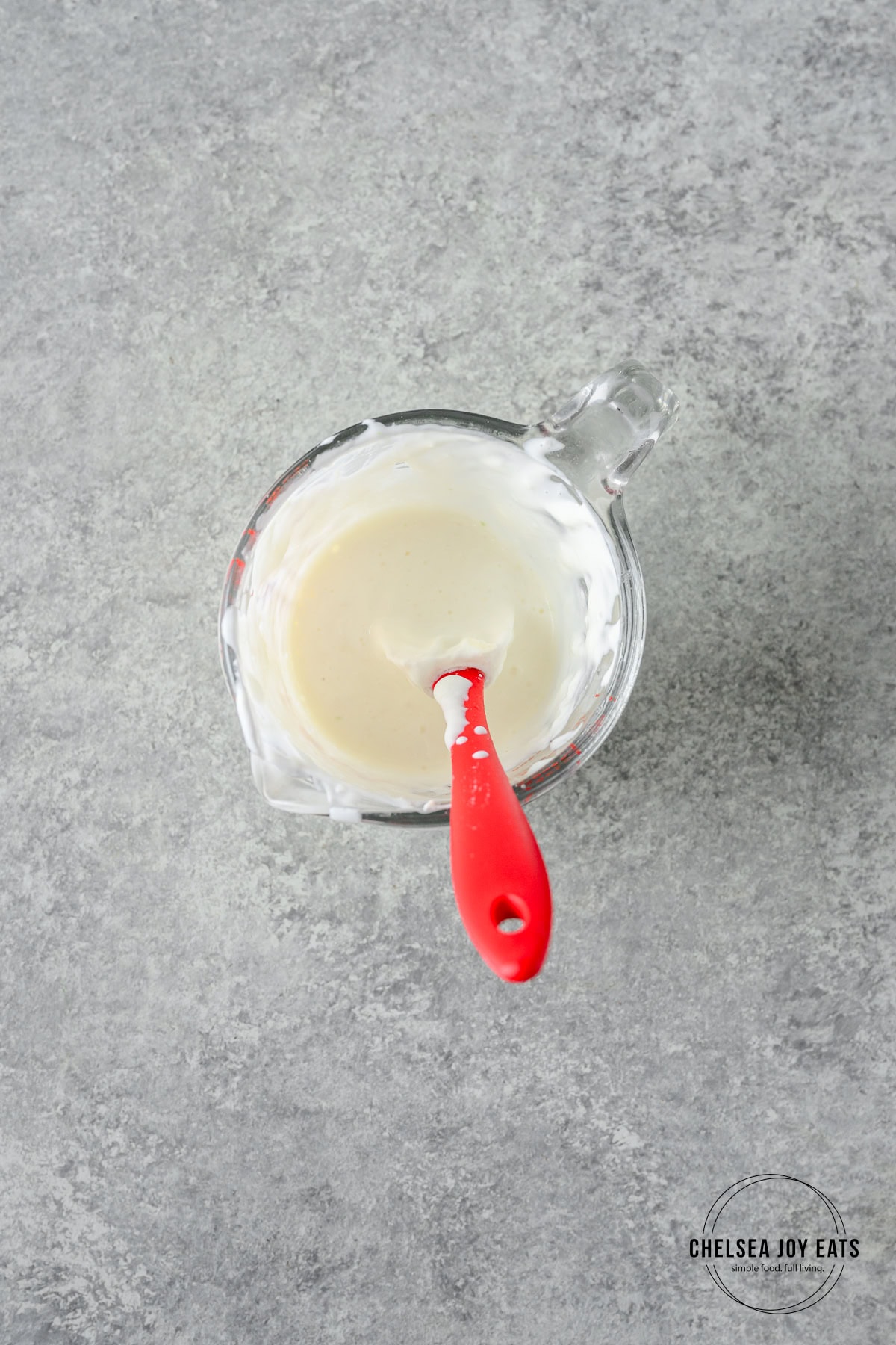 Yogurt garlic sauce stirred together in a small glass bowl with a silicon spatula.